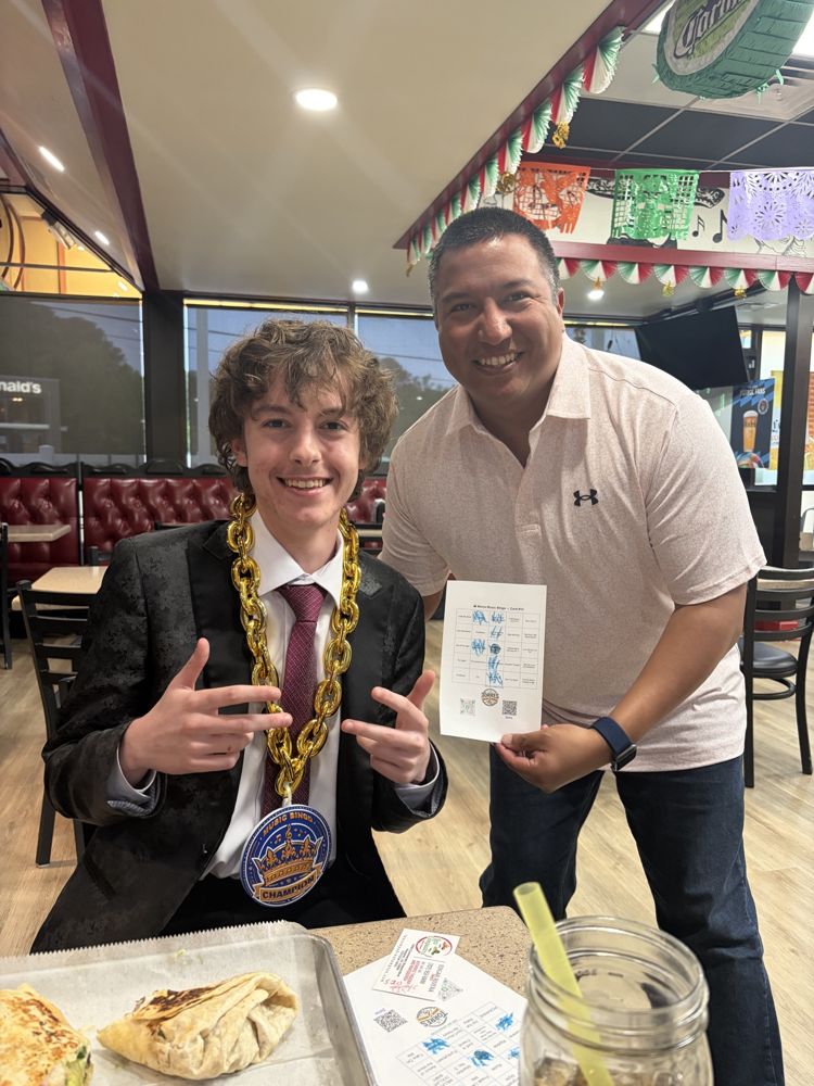 A Music Bingo champion wearing the gold chain and medal, with the host holding the winning card