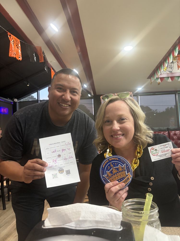 A winner holding the Music Bingo champion medal next to the host with her winning card